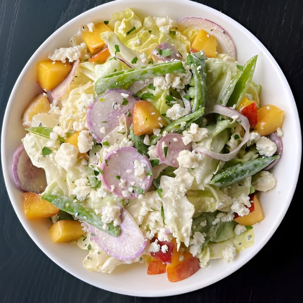 A white bowl of DAMNFiNE pizza's fresh salad with lettuce, radishes, peppers, and feta cheese.
