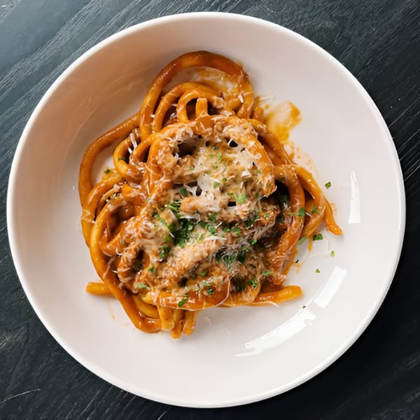 DAMNFiNE pizza's bucatini pasta with red sauce, shredded cheese, and fresh herbs in a white bowl.