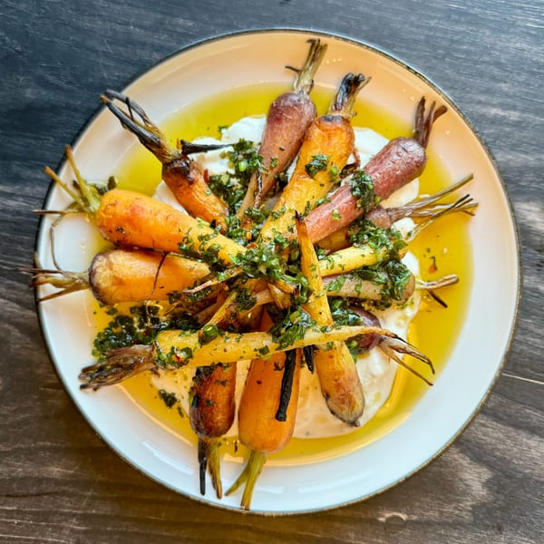 Roasted carrots with green herbs and olive oil on a white plate, from DAMNFiNE pizza.